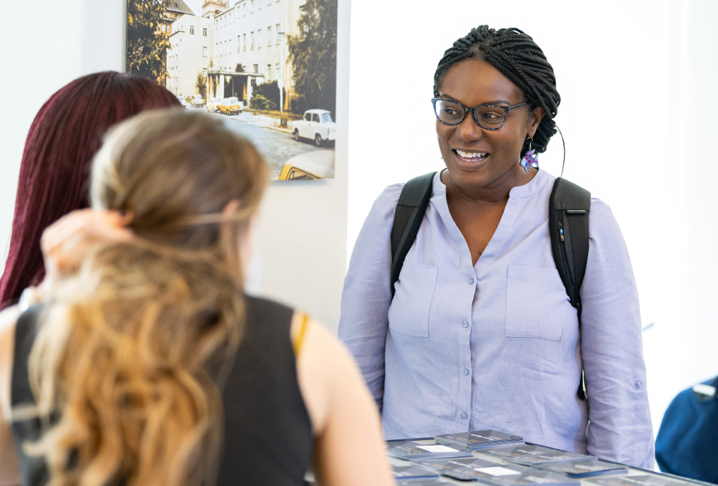 An event exhibitor with a bag on her shoulder presents information at her booth.