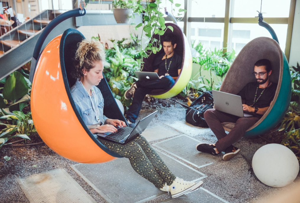 A group of people working on laptops while seated in a modern indoor swing.