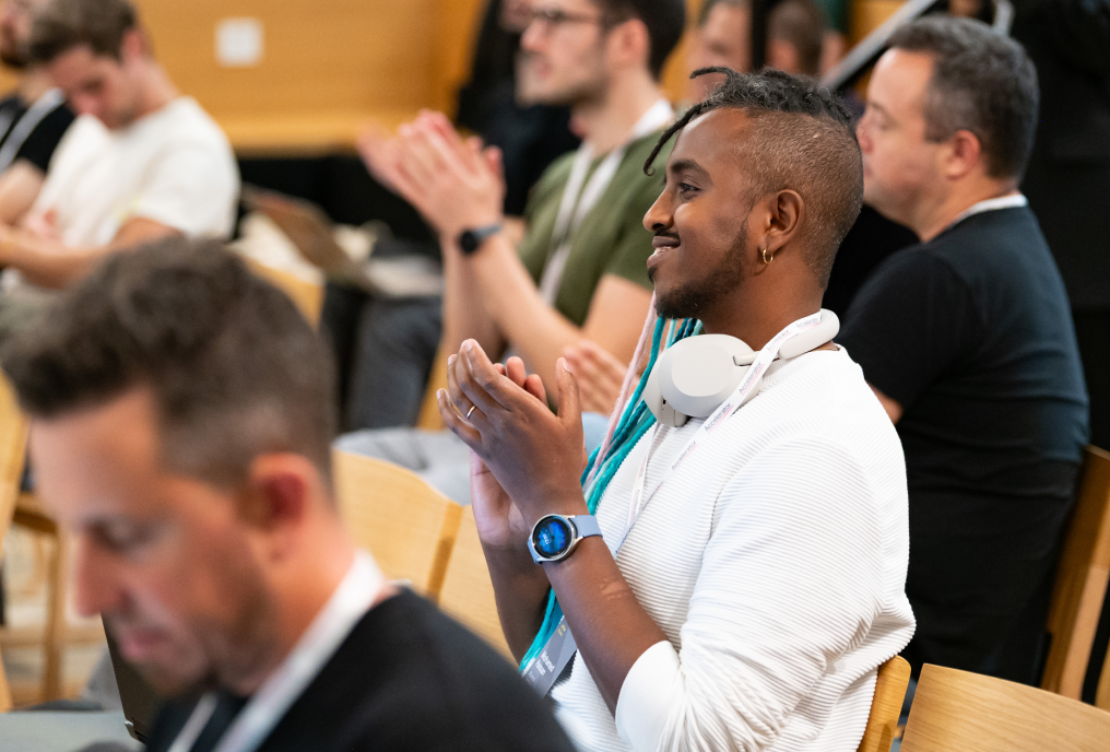 Someone from the audience, wearing headphones, is clapping along with the others.