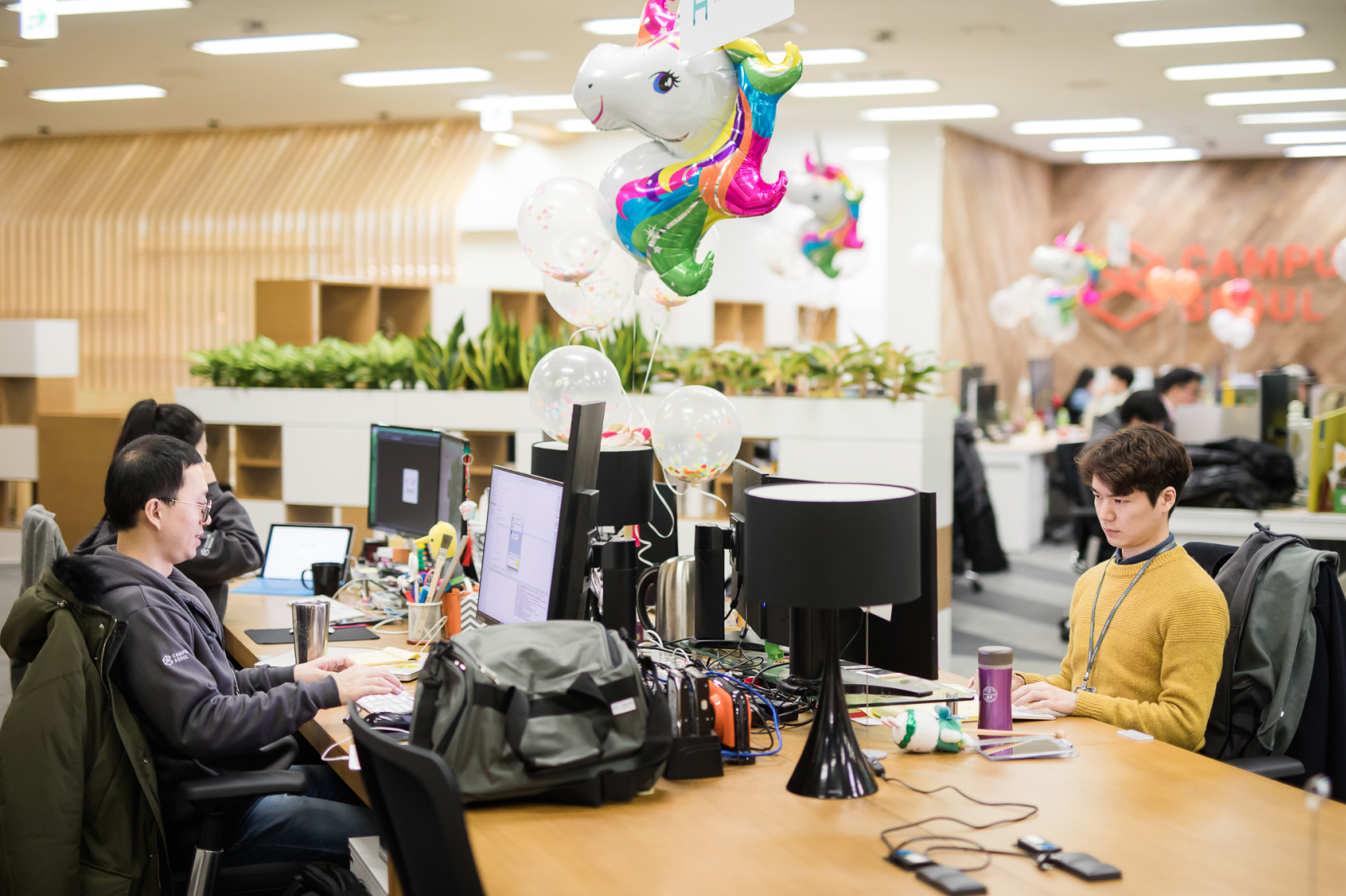 Group of young people work in a modern office with Rainbow Unicorn Balloon Bouquet on desk